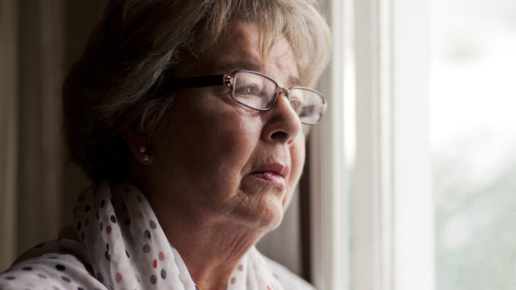 Lonely senior woman looking out window