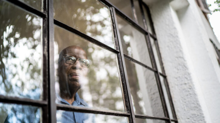 Senior man looking through the window at home