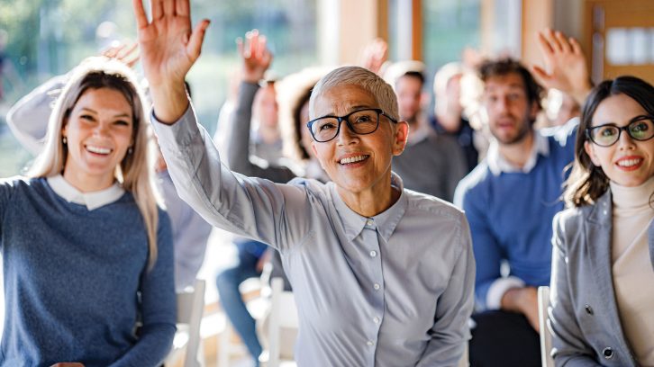 Happy senior businesswoman raising her hand to ask a question during an education event in board room